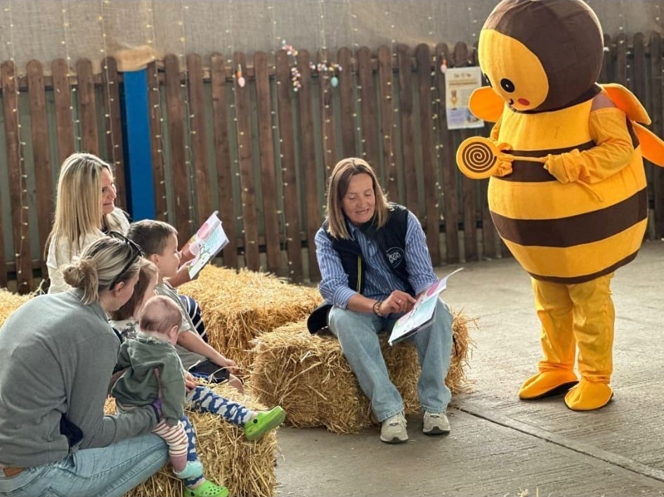 lady sat on hay bale with large bee next to her reading a mindful bee book