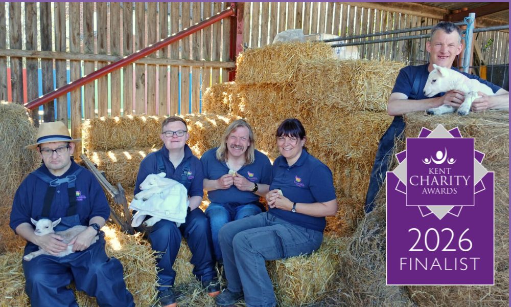 People in a barn holding lambs with Kent Charity Awards symbol